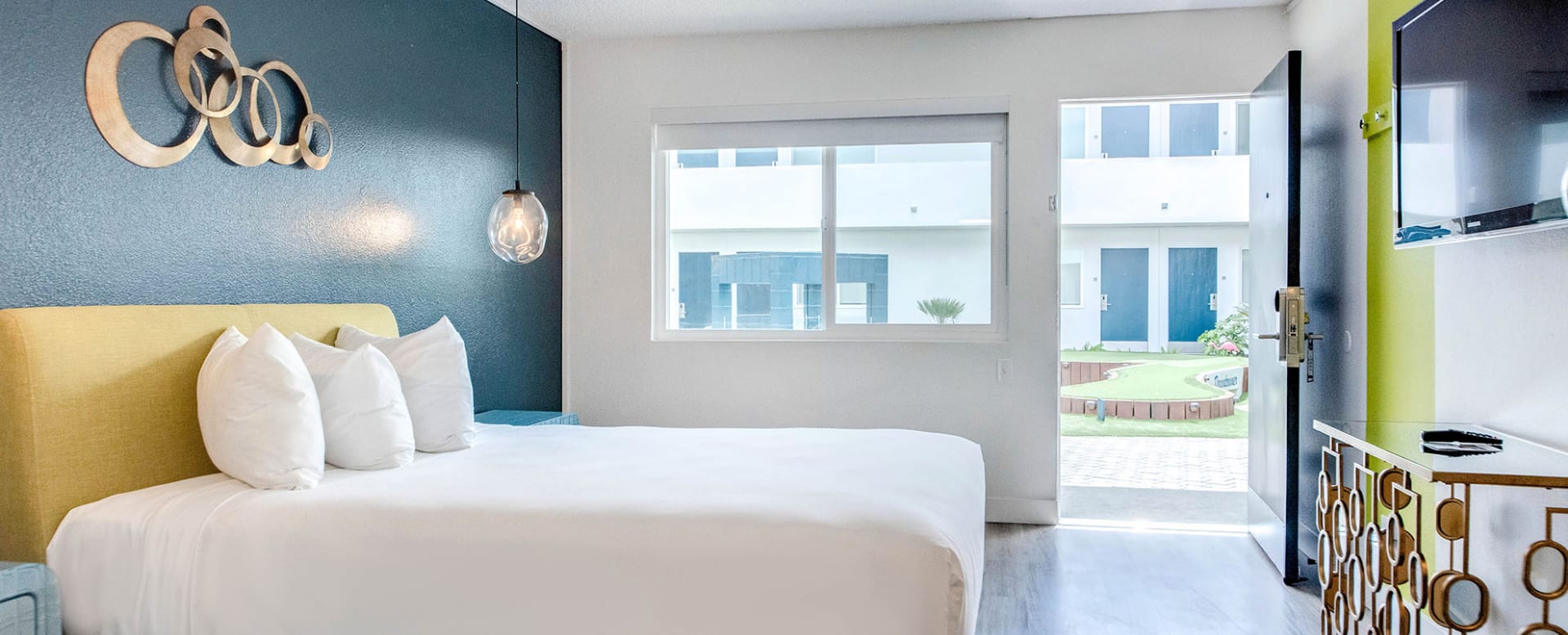 A hotel room with a bed, window, door, and TV.